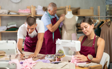 Working day in sewing workshop, textile industry. Girl master sew clothes in sewing machine, guy...