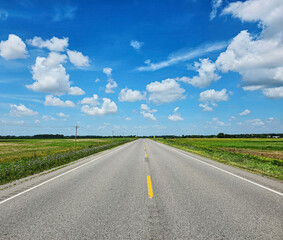 Beautiful and serene country road leading into the forest rural landscape background of a summer road trip with blue sky and white puffy clouds on a bright sunny day