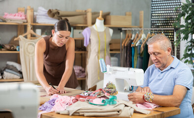 Family business, production of clothes - tailor showroom. Mature man tailor sew and work in cloth...