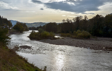 Serene autumn landscape featuring a tranquil Cheremosh river surrounded by lush greenery with...