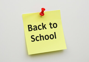 Yellow sticky note with back to school message and red push pin on white surface.
