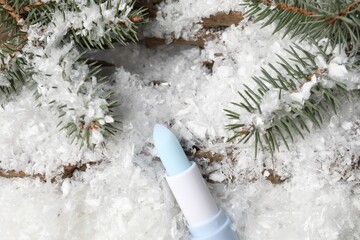Moisturizing lip balm and fir tree branches on artificial snow, flat lay. Winter care