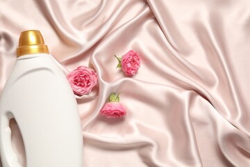 Bottle of fabric softener and flowers on beige cloth, flat lay. Space for text
