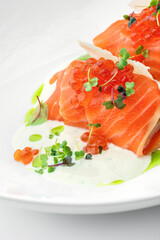 Salmon rolls and red caviar with sauce and greens on plate isolated on white background. Fish and seafood, close up, top view
