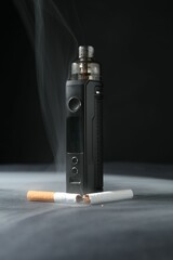 Electronic smoking device and broken cigarette in smoke on dark table against black background,...