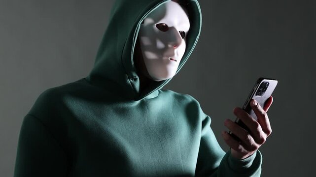 Anonymity. Masked man with smartphone on grey background