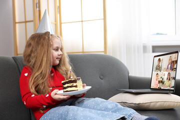 Celebrating birthday online. Little girl with cake having video call with friends via laptop at home