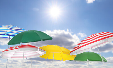 Different bright beach umbrellas against blue sky on sunny day