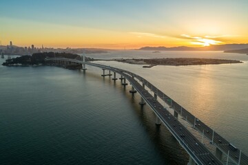 Obraz premium Aerial view of the San Francisco-Oakland Bay Bridge in California, USA, at sunset. Cars travel across the bridge, connecting San Francisco to Oakland.