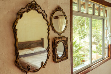 Three ornate vintage mirrors reflecting a rustic bedroom with wood furniture and large window....