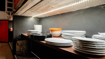 Rustic kitchen shelf with stacked white and black plates, bowls, and LED strip lighting, modern cozy design.