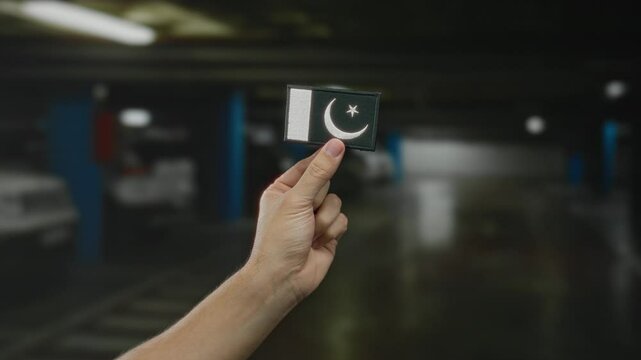 Man holding pakistani flag embroidery in indoor parking area, displaying national pride in a modern setting.