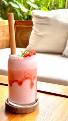 Vertical image of a colourful fresh pink strawberry smoothie drink served with bamboo straw outdoor at daytime on a terrace during a summer holiday on Bali in Indonesia.