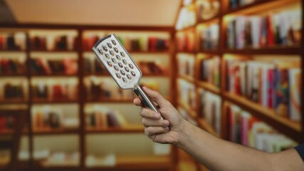 Man holding grater in a library setting surrounded by books highlighting a unique juxtaposition of culinary tool in an indoor academic environment