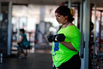 Beautiful overweight Latina woman lifting dumbbells in a gym, wearing a green 80s-style t-shirt,...