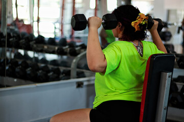Beautiful overweight Latina woman exercising with dumbbells, looking at herself in the mirror at a...
