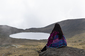 young woman sitting watching colombian sumapaz landscape with a big lake and mountains at background