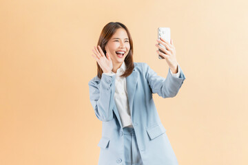 Confident Asian businesswoman using smartphone at video call friends online through the internet on beige color background.