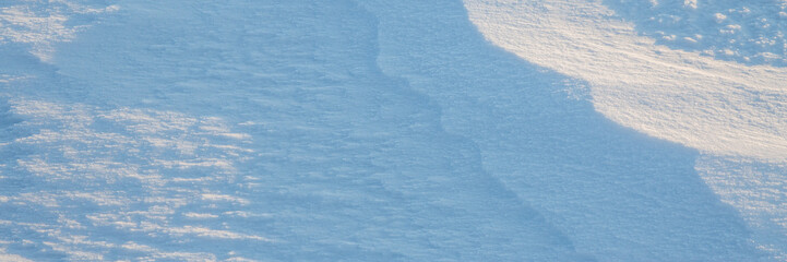 Beautiful winter background with snowy ground. Natural snow texture. Wind sculpted patterns on snow surface. Wide panoramic texture for background and design.