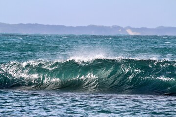 Naklejka premium Ocean wave about to break with spray land in the distance