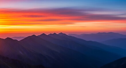 Obraz premium Breathtaking vista of mountain range silhouettes bathed in the warm glow of a vibrant sunrise sky with orange, red, and blue hues.