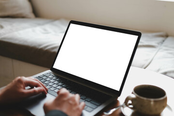A person typing on a laptop with a blank white screen in a cozy and comfortable workspace with a coffee cup. A versatile content mockup.