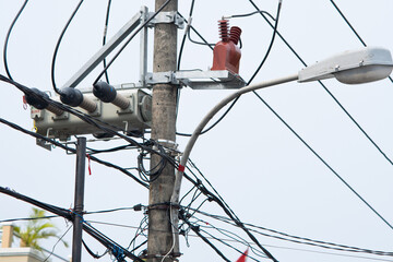A typical electricity pole in Indonesia, heavily laden with numerous power lines, a transformer,...