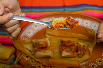 Hands of a person cutting a tamale with a fork. Tamale, typical Mexican food.