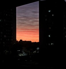 A stunning and colorful sunset unfolds between two tall urban buildings in Sao Paulo, creating a striking contrast between the warm light of the sky and the shadows of the structures.