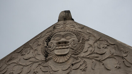 An intricate stone carving of a stylized traditional face, likely a guardian figure, adorning an...