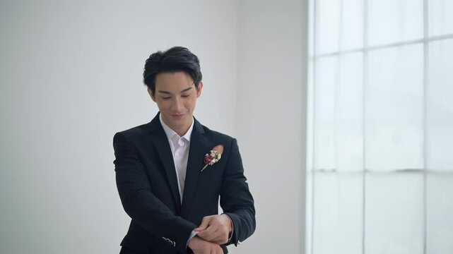 Asian Groom fixing his cufflinks. Handsome groom dressed in black formal suit getting ready for wedding. Elegant groom wedding fashion.