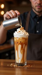 Barista pouring cream into caramel iced latte with whipped cream topping