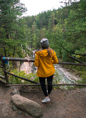Young woman in yellow jacket gazes over river and forest landscape in early morning light