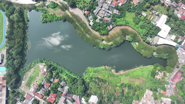 a lake covered in green plants located in the middle of the city and has a flow to the river to dam flooding