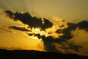 Golden sun paints the evening sky over a beautiful mountain landscape, silhouetted by the vibrant hues of a summer sunset or sunrise