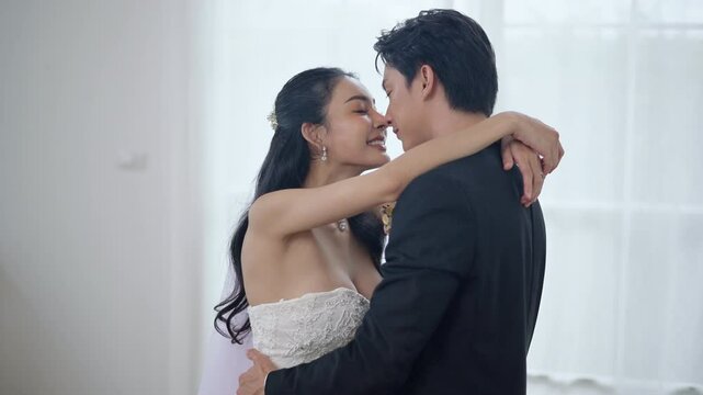 A happy Asian couple in wedding attire, hugging each other and smiling joyfully, bride and groom are having fun together in a white wedding dress and suit, both of them dancing to romantic songs