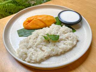 Delicious Thai mango sticky rice with fresh mango pieces on a plate with wooden table background.