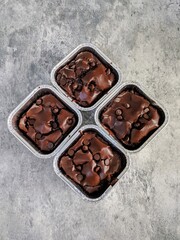 Top view of four fudgy chocolate brownies in square foil containers, topped with chocolate chips,...