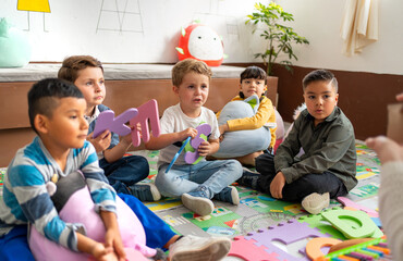 A diverse group of preschool kids engages with the teacher exploring colorful letters during class...