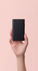 A hand holds a small, black rectangular power bank against a pale pink background