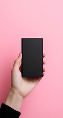 Hand holding a black rectangular power bank against a pink background