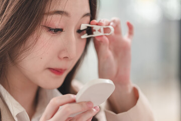 Young woman applies eyelash curler while checking reflection in compact mirror to enhance eye makeup look