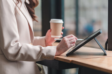 Professional woman engages with digital tablet while enjoying coffee at modern workspace