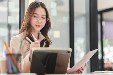 Young professional engages in creative work with tablet and notepad in modern office environment