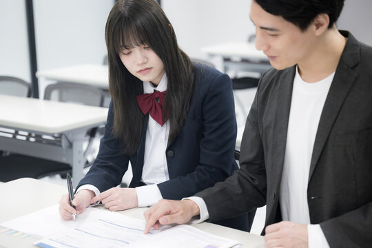 学生の面談や個別指導、進路指導の塾などのイメージの先生と生徒 目指せ大学受験の合格~!机で勉強