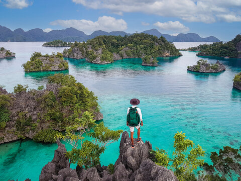 Adventure traveler hiking hilltop with panoramic view of turquoise ocean and Sombori rocky islands, Indonesia. Great for summer and travel stock.