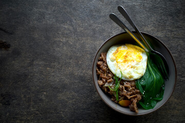A bowl of food with a fried egg, savory beef and a green vegetable