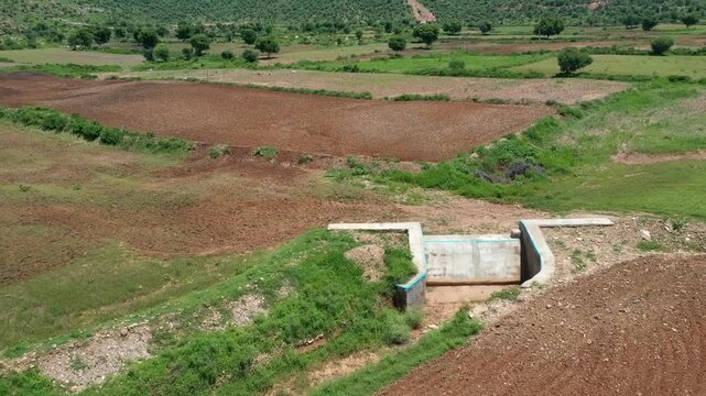 Aerial view of agricultural fields in Telangana with brown and green plots divided by narrow paths surrounded by scattered trees and low hills under bright daylight in countryside setting