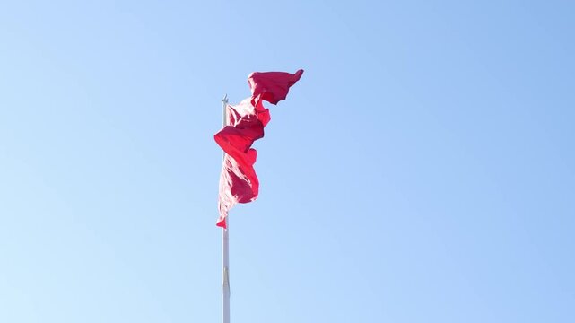 A red flag of Kyrgyzstan waving against a clear blue sky. The flag features a yellow sun with 40 rays in the center, symbolizing the 40 tribes of Kyrgyz people.