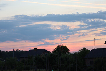 A sunset over a Ukrainian village, where the outlines of houses and trees are visible against the...